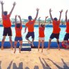 Gruppo di persone in maglia arancione salta davanti a una piscina.
