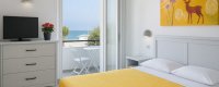 Camera con letto giallo, TV e balcone.