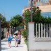 Persone camminano verso la spiaggia, palme e edificio sulla destra.