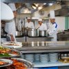 Cuochi lavorano in cucina con grandi pentole e piatti pronti.