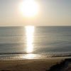 Mare calmo e sole al tramonto che si riflette sull'acqua, con una spiaggia in primo piano.