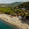 Vista aerea di una spiaggia con ombrelloni bianchi e vegetazione circostante.