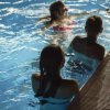 Persone nuotano in piscina dal bordo illuminato.