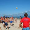 Persone giocano a beach volley su una spiaggia soleggiata.