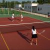 Un campo da tennis all'aperto con persone che giocano a tennis doppio sotto il sole.