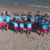 Gruppo di persone in magliette azzurre e pantaloncini rosa sulla spiaggia, sorridenti in posa.