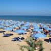 Spiaggia con numerosi ombrelloni blu e molte persone sul bagnasciuga.