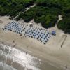 Vista aerea di una spiaggia con ombrelloni blu e vegetazione circostante.