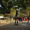 Parco giochi con altalene, scivoli e bambini che giocano sotto alberi ombrosi.