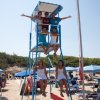 Persone su una torretta di bagnino in spiaggia con ombrelloni blu.