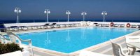 Piscina con lettini e lampioni, vista sul mare all'orizzonte.