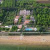 Spiaggia con lettini, strada alberata e un edificio immerso nel verde.