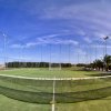 Campo da tennis all'aperto con rete e recinzione, circondato da palme.