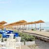 Spiaggia con ombrelloni di paglia, lettini, e una zona caffè con sedie blu e bianche.
