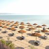 Spiaggia con file di ombrelloni di paglia e lettini su sabbia dorata, vista sul mare calmo.