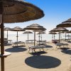 Spiaggia con ombrelloni di paglia e lettini vuoti sotto un cielo limpido.