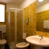 Bagno con doccia in vetro, lavabo, bidet e pareti con piastrelle gialle.
