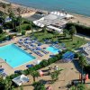 Vista aerea di un resort con piscina, sdraio e ombrelloni vicino alla spiaggia.