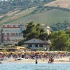 Spiaggia affollata con ombrelloni e colline sullo sfondo.