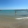 Spiaggia con persone in acqua vicino a barriere frangiflutti sotto un cielo limpido.