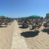 Spiaggia affollata con ombrelloni verdi e arancioni.