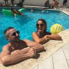 Due persone sorridenti al bordo di una piscina con un pallone giallo.