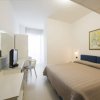 Stanza con letto matrimoniale, TV su scrivania e quadro appeso. Mobili bianchi e pareti chiare.