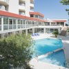 Piscina all'aperto circondata da un edificio bianco con balconi e vegetazione.