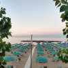 Spiaggia al tramonto con ombrelloni turchesi e mare calmo, vista tra alberi.