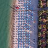 Spiaggia con ombrelloni blu e villette viste dall'alto.