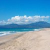 Spiaggia sabbiosa con mare azzurro e montagne in lontananza.