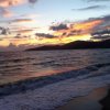 Tramonto su una spiaggia con onde e cielo colorato.