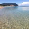 Spiaggia di ciottoli con mare cristallino e colline sullo sfondo.