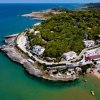 Baia con vegetazione, strutture costiere, e spiaggia con ombrelloni.