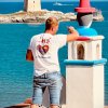 Un uomo dipinge una colonnina colorata vicino al mare, con una torre in lontananza.