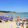Spiaggia affollata con ombrelloni blu, bagnanti e pedalò sul mare.