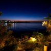 Vista notturna sul mare con luci e palme illuminate.