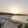 Spiaggia al tramonto con ombrelloni, barche e alcune persone sulla sabbia.