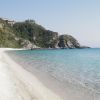 Spiaggia sabbiosa con mare azzurro e scogli.