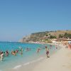 Spiaggia affollata con bagnanti e case sulla costa rocciosa.