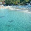 Spiaggia deserta con acque cristalline e lettini blu.