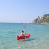 Persona in kayak rosso, mare e scogliera sullo sfondo.