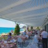 Persone pranzano all'esterno in riva al mare sotto una tettoia bianca.