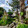 Giardino con statua, fiori e palme sotto un cielo nuvoloso.
