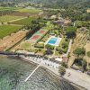 Veduta aerea di un complesso con piscina, campi da tennis e giardini vicino al mare.