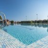 Una piscina con acqua limpida e una scaletta in metallo, ombrelloni sullo sfondo.