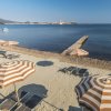 Spiaggia con ombrelloni a righe e lettini, un molo si estende verso il mare.