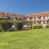 Un edificio a tre piani circondato da un prato verde, con balconi e piante in primo piano.