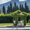 Una piscina con un gazebo ricoperto di piante, alberi sullo sfondo e una montagna in lontananza.