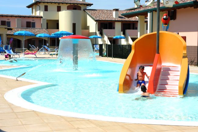 Piscina con scivolo arancione, giochi d'acqua e ombrelloni blu.